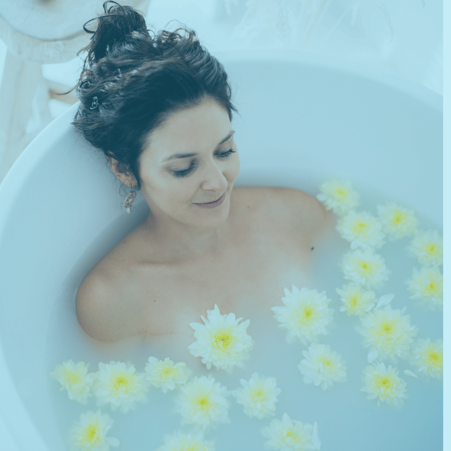 person with bun on head lying in bathtub surrounded by yellow and white flowers