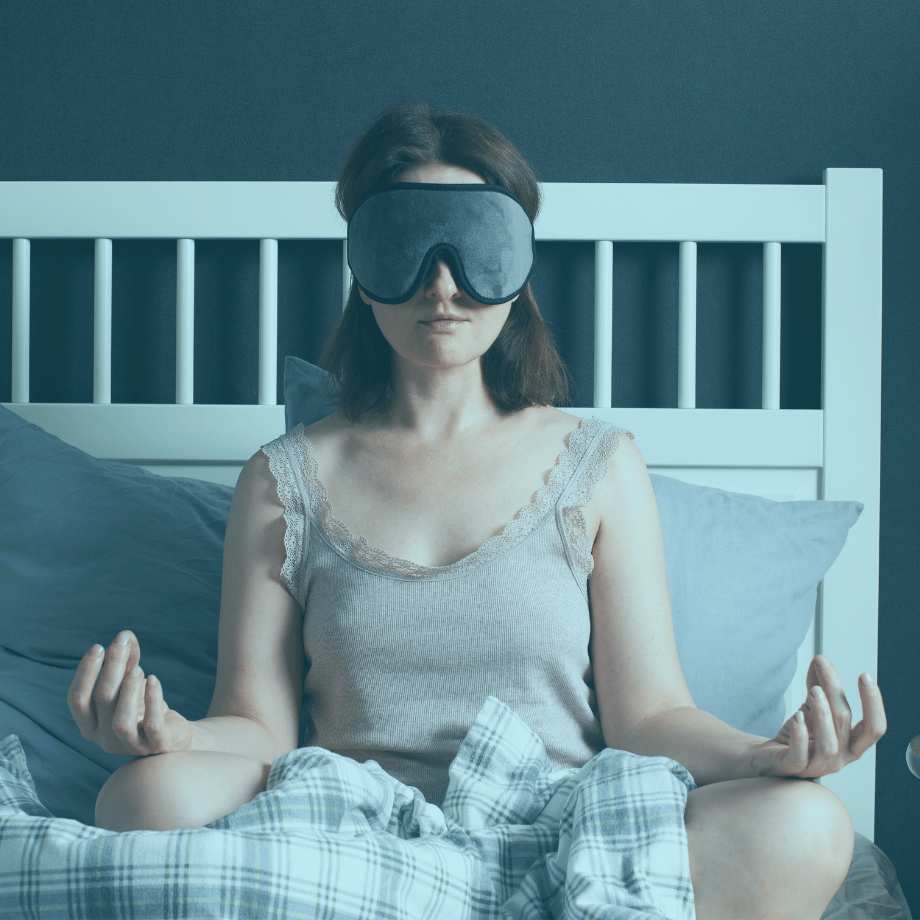 Woman in facemask with hands in lotus pose meditating in bed