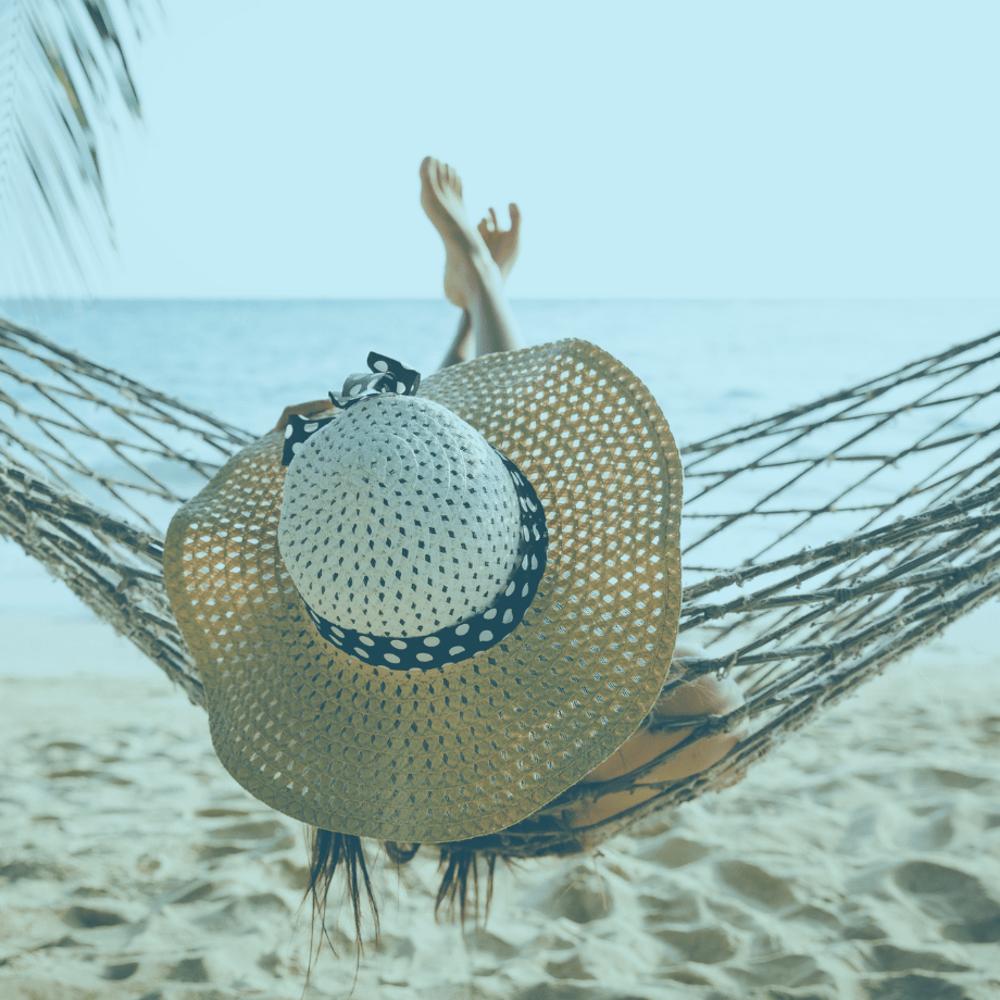 Lady with white hat leaning into hammock at the beach